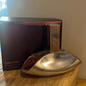 Euphoria Eau de Parfum från Calvin Klein 100ml - Elegant parfymflaska i silver och vinrött med doftnoter av granatäpple, persimon och grön ackord. Mellannoter av svart orkidé, lotus och champaca, samt basnoter av mahogny, amber och svart viol. Perfekt för den som söker en sofistikerad och sensuell doft. Nypris: 850kr