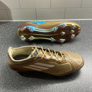 Adidas F50 Messi x Bad Bunny - ADIDAS F50 MESSI X BAD BUNNY ELITE FG - CARDBOARD/VIT/TURKOS LIMITED EDITION.          Säljer ett par helt oanvända Adidas F50 fotbollsskor då jag inte behöver fler än vad jag redan har. orginalpris på unisport nu: 3049kr 