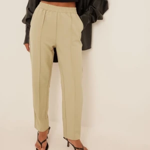 Beige kostymbyxor med resårmidja - Snygga beige kostymbyxor med resårmidja och rak passform. Perfekta för en stilren look, dessa byxor har en klassisk design med pressveck framtill.