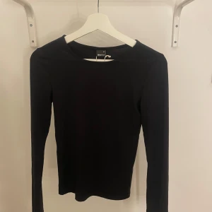 Svart långärmad topp från Gina Tricot - Säljer en stilren svart långärmad topp från Gina Tricot. Helt oanvänd och som ny! Det är även soft touch så väldigt skön. Toppen har en mjuk känsla och rund halsringning, perfekt för en minimalistisk look. Passar bra till både jeans och kjol. 🖤
