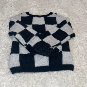 Svart och vit rutig stickad tröja - Säljer en mysig stickad tröja med ett stort rutmönster i svart och vitt. Tröjan har långa ärmar och en rund halsringning. Perfekt för kyliga dagar!