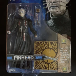 Pinhead Actionfigur - Denna actionfigur föreställer Pinhead, en ikonisk karaktär från skräckgenren. Figuren är detaljerad med en svart dräkt och de karakteristiska gyllene nålarna i huvudet. Förpackningen inkluderar även tillbehör för att återskapa scener från filmen. Perfekt för samlare och skräckfantaster!