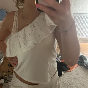 Vit oneshoulder topp med spetsdetaljer - Säljer en superfin vit oneshoulder topp med spetsdetaljer. Perfekt för sommarens fester eller en dag på stan. Toppen är i bra skick och väldigt bekväm att bära.