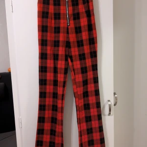 Röd och svart rutig byxa med dragkedja - Säljer ett par fantastiska röda och svarta rutiga byxor med dragkedja framtill. Byxorna är högmidjade och har en rak passform. Älskar dessa men har tyvärr växt ur dem. Materialet är stumt och ej stretchigt.