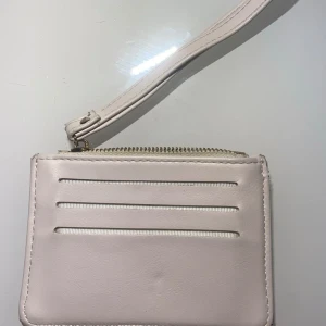 Beige plånbok med dragkedja - Säljer en stilren beige plånbok med dragkedja. Den har flera kortfack och en praktisk handledsrem. Perfekt för att hålla ordning på kort och kontanter. Passar till alla tillfällen! 💖