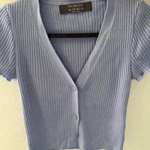 Ljusblå ribbad kortärmad topp från Primark - Säljer en superfin ljusblå ribbad topp från Primark. Den har korta ärmar och en v-ringad design med knappar framtill. Perfekt för vår och sommar!