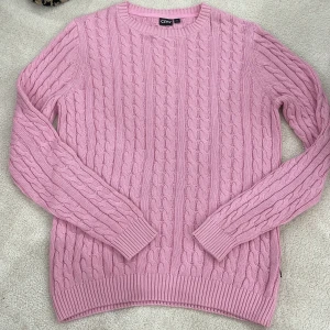 Rosa stickad tröja från CRW - Säljer en superfin rosa stickad tröja från CRW. Den har ett klassiskt flätmönster och är perfekt för både höst och vinter. Tröjan är långärmad och har ribbade muddar vid ärmslut och nederkant. Den är i storlek M och är i nyskick. Perfekt för att hålla sig varm och snygg! 💖