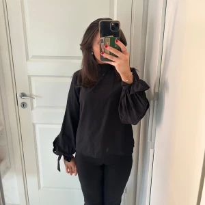 Svart blus med knytband - Säljer en elegant svart blus med långa ärmar och knytband vid ärmsluten. Passar perfekt för både vardag och fest! Blusen är aldrig använd. Den är i storlek 34 men passar mig som är i storlek 36💖 pris går att diskutera🫶🏽