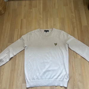 Beige tröja från Lyle & Scott - Säljer en snygg beige tröja från Lyle & Scott i storlek S. Den har en klassisk v-ringning och är prydd med deras ikoniska logga i gult och svart på bröstet. Perfekt för både vardag och lite finare tillfällen. Tröjan är i bra skick och supermjuk!