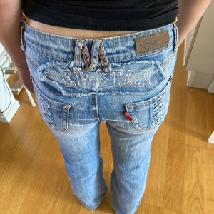Blå jeans med detaljer - Säljer ett par blå jeans med coola detaljer. De har en låg midja och är bootcut.(ser inte ut så för att dem är för stora för min syrra, men dem är tyvärr för små på mig nu så min syrra fick ställa upp att vara model)Jeansen har slitna kanter vid bensluten och snygga broderade detaljer på fickorna. Perfekta för en avslappnad och trendig look!