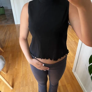 Svart ärmlös topp från Zara - Säljer en svart ärmlös topp från Zara i storlek M. Toppen har en vågig kant vid nederkanten som ger en söt detalj. Perfekt för både vardag och fest!