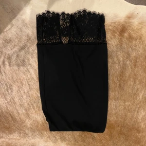 Svart kjol med spetsdetaljer - Säljer en elegant svart kjol med vacker spets upptill. Kjolen är perfekt för festliga tillfällen och har en tight passform som framhäver figuren. Den är gjord i ett mjukt och bekvämt material som känns skönt mot huden. Perfekt för en utekväll eller en speciell middag!
