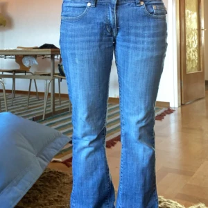 Blå jeans från Victoria Beckham för Rock & Republic - Säljer ett par snygga och unika blå jeans från Victoria Beckham för Rock & Republic. De har en bootcut-stil, samt är lågmidjade och är dekorerade med coola broderade kronor på bakfickorna. Jeansen är i storlek 28 och är tillverkade i USA. Perfekta för en avslappnad men stilren look!