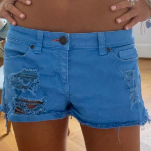 Blå jeansshorts med slitningar - Säljer dessa jeansshorts i en sååå fin blå färg!💙💙 Midjemått: 40cm Frakt tillkommer.