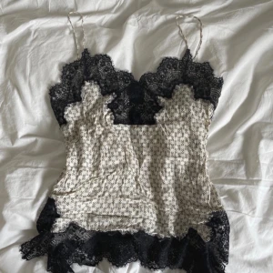 Blommig linne med spetsdetaljer - Säljer ett supersött linne med blommigt mönster och svarta spetsdetaljer. Linnet har tunna axelband och är perfekt för sommaren. Det är gjort av ett lätt och luftigt material, vilket gör det bekvämt att bära. Passar både till vardags och fest!