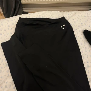Svarta leggings från Gymshark - Säljer ett par svarta leggings från Gymshark i storlek L. De är tillverkade av 78% återvunnen polyester och 22% elastan, vilket gör dem superstretchiga och bekväma för träning. Perfekta för gymmet eller yoga! 🖤