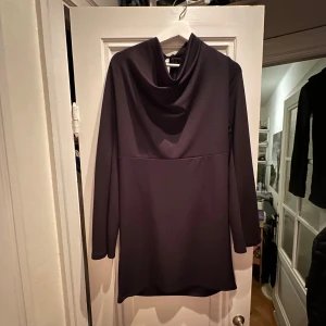 Svart klänning - Säljer en elegant svart långärmad klänning med en draperad krage. Klänningen är aldrig använd och har en normal passform.