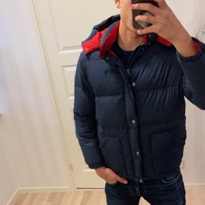 Mörkblå dunjacka från Polo Ralph Lauren - Säljer en snygg mörkblå dunjacka från Polo Ralph Lauren i storlek L i ungdomstorlek som passar Xs/ och kanske S i vuxenstorlek. Funkar perfekt om man är 170-177 cm lång! Jackan har en röd insida och en praktisk huva som går att ta av. Den är långärmad med dragkedja och knappar framtill. Perfekt för kalla vinterdagar! 🧥❄️