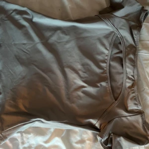 Grå kortärmad topp - Säljer en stilren grå topp i mjukt material. Den har korta ärmar och en enkel design som passar perfekt till vardags eller träning. Toppen är i bra skick och har en normal passform.