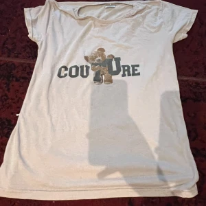 Beige t-shirt med nalletryck - Säljer en beige t-shirt med ett sött nalletryck och texten 'COUTURE' på framsidan. T-shirten är kortärmad och i ett mjukt material, perfekt för en avslappnad stil. Passar bra till jeans eller shorts för en casual look.