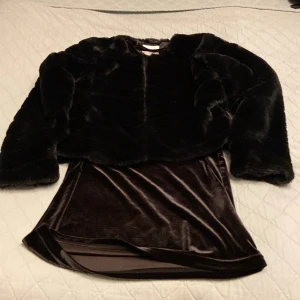 Svart pälsjacka och svart klänning - Säljer en supermjuk och fluffig svart pälsjacka från Lindex Kids tillsammans med en svartklänning i ett sammets aktivt material. Jackan har långa ärmar och en enkel design som passar till alla outfits. Jackan och klänningen är i mycket fint skick och passar aktiviteter under höst och vinter!