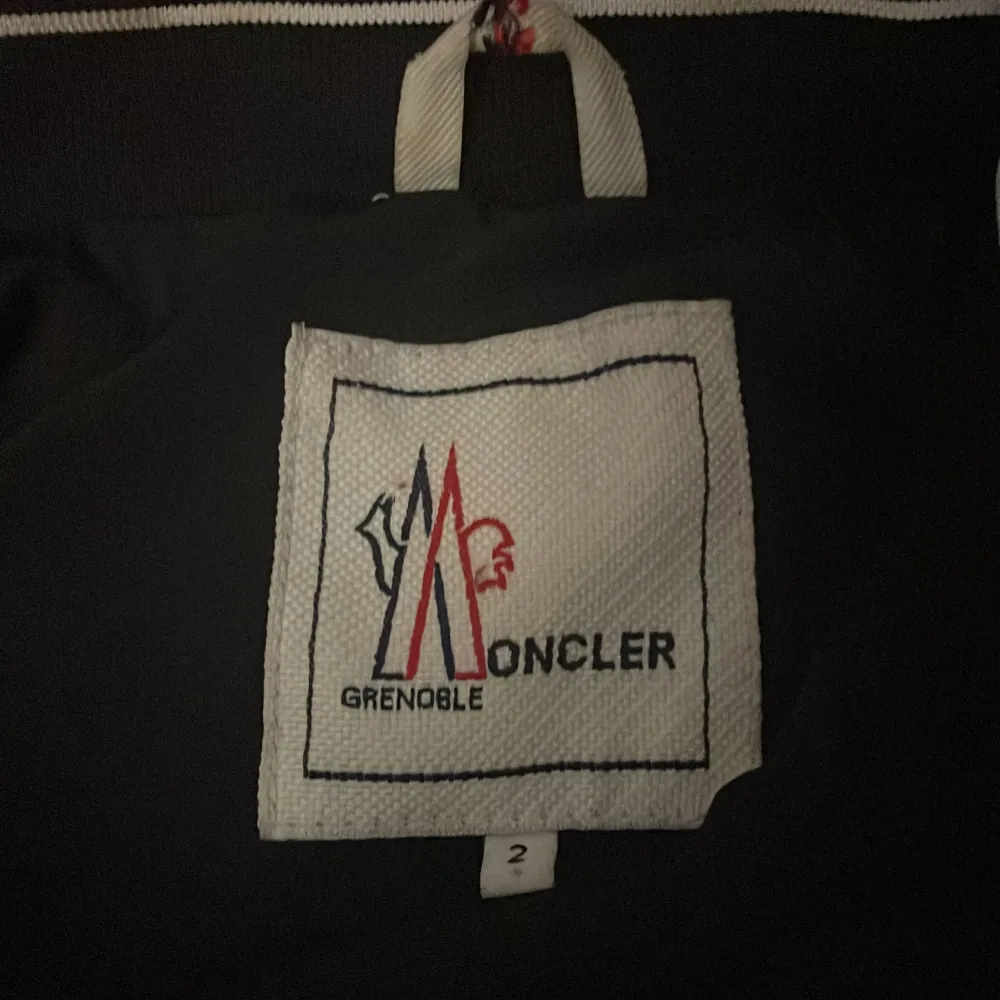 Säljer en snygg svart jacka från Moncler i mycket bra skick. Den har en dragkedja framtill och en huva med Moncler-logga. Perfekt för höst och vår, med en stilren design och hög kvalitet. Passar både till vardags och lite finare tillfällen.. Takit.