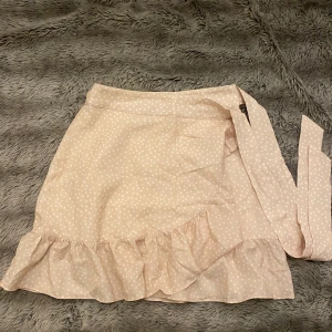 Beige prickig kjol med volang - Superfin beige kjol med vita prickar och volangdetalj längst ner. Den har en omlott-design med knytband i midjan, vilket ger en söt och feminin look. Perfekt för vår och sommar! 🥰