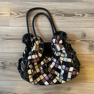 Pastellfärgad axelväska - Säljer en unik axelväska med ett coolt rutigt mönster i svart, vit, lila och beige. Väskan har en glansig finish och är gjord av syntetmaterial. Perfekt för att ge din outfit en färgglad touch! 👜💐🌟