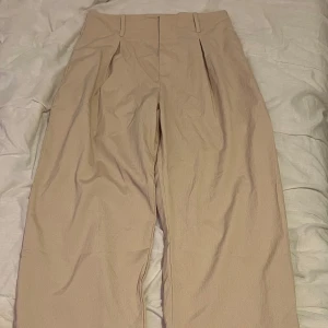 Beige kostymbyxor - Säljer ett par stilrena beige kostymbyxor i mycket bra skick. De är högmidjade med en loose passform, perfekta för både kontoret och mer avslappnade tillfällen. Byxorna har en klassisk design med veck framtill och hällor för bälte. Superbekväma och lätta att matcha med olika toppar!säljs för 70