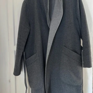 Grå kappa från 365 - Säljer en stilren grå kappa från 365 i ullblandning. Den har långa ärmar och ett bälte i midjan för en snygg passform. Perfekt för höst och vinter! 🧥