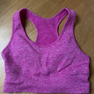 Rosa ribbad sporttopp - Säljer en snygg rosa ribbad sporttopp i mycket bra skick. Perfekt för träning med sin bekväma passform och brottarrygg. Materialet är stretchigt och andas bra, vilket gör den idealisk för intensiva pass. Toppen är i storlek dam S och har en härlig färg som piggar upp vilken träningsoutfit som helst!