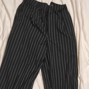 Svarta randiga byxor - Säljer ett par snygga svarta byxor med vita ränder. De har en loose passform och är perfekta för både vardag och fest. Byxorna är högmidjade och ger en stilren look. Perfekta för höst och vår!