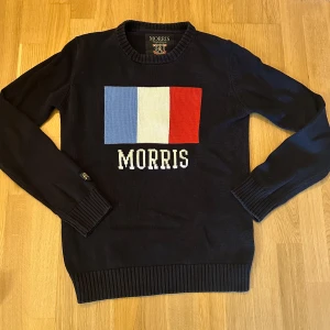 Mörkblå tröja från Morris - Säljer en snygg mörkblå tröja från Morris med ett stort tryck av den franska flaggan och texten 'Morris' på framsidan. Tröjan är i bra skick och har långa ärmar med ribbade muddar. Perfekt för höst och vinter! Lite smått blekt i kragen (se bild 3 och sista bilden). Storlek S men skulle säga att den är stor i storleken  