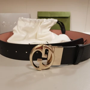 Svart skärp från Gucci med guldspänne - Säljer ett elegant svart skärp från Gucci i skinn med ett stort, glänsande guldspänne. Perfekt för att ge en lyxig touch till vilken outfit som helst. Skärpet är i fint skick. Passar perfekt för sommarens fester! 🌟