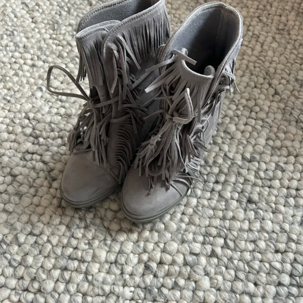 Säljer ett par snygga grå boots i mocka med fransar och snörning. De har en bekväm kilklack och är perfekta för höst och vår. Skorna är i mycket bra skick och passar både till vardags och fest. 💗. Skor.