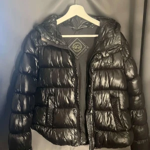 Svart pufferjacka från Superdry - Säljer en snygg svart pufferjacka från Superdry i storlek L. Jackan är perfekt för kalla dagar med sin vadderade design och har en praktisk huva. Den passar mig bra som brukar ha 36-38 men den är liten i storlek!🙌🙌 Skriv för fler bilder!