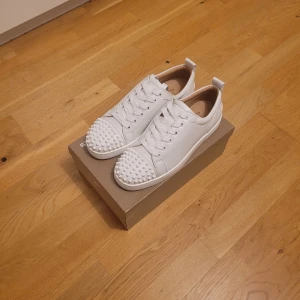 Christian Louboutin  - Säljer ett par vita sneakers från Christian Louboutin i nytt skick. Skorna har coola nitar på tån och den klassiska röda sulan. Perfekta för att ge din outfit en edgy touch! Kommer med originalkartong och dustbag.