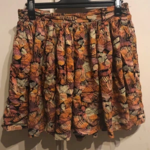 Mönstrad kjol från Jeane Blush - Säljer en superfin mönstrad kjol från Jeane Blush i storlek M. Kjolen har ett färgglatt mönster i orange, rosa och svart med en bekväm resår i midjan. Perfekt för både vardag och fest! 🧡