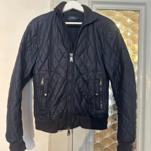Svart quiltad jacka från Polo Ralph Lauren - Säljer en snygg svart quiltad jacka från Polo Ralph Lauren i storlek S. Jackan har dragkedja och ribbade muddar vid ärmslut och nederkant. Perfekt för höst och vår! 🖤