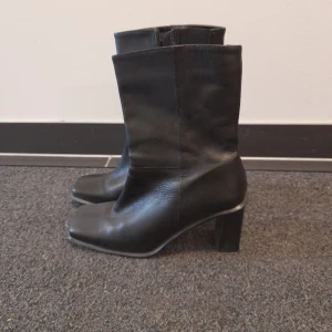 Svarta boots med klack - Snygga svarta boots i äkta skinn med en bekväm klack och dragkedja på sidan. Perfekta för höst och vinter, dessa boots har en stilren design. De är i bra skick och passar både till vardags och fest.