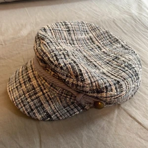 Newsboy cap från Loevenich - Snygg newsboy keps från Loevenich i en mix av svart, vit och beige. Den har en cool flätad detalj och en knapp på sidan. Perfekt för höst och vår när du vill ha en stilren look. Materialet är en blandning av nylon, polyester och akryl. Original pris runt 300 kr nytt pris 100kr🌟