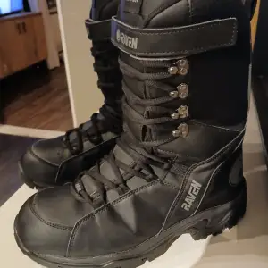 Säljer ett par robusta svarta boots från Raven i storlek 46. De är gjorda av PU-läder med en innerfoder av TPU-membran, vilket gör dem både vattentäta och andningsbara. Perfekta för vintern med snörning och en hög design för extra stöd. Lättvikt som gör dem lätta att gå i. Nypris 1799