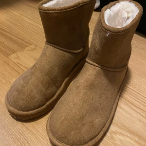 Bruna boots från Monki - Säljer ett par mysiga bruna boots från Monki i storlek 38/39. De är gjorda i mocka med en mjuk, vit foder inuti som håller fötterna varma. Perfekta för höst och vinter! Sulan är i bra skick och ger bra grepp. Helt nya aldrig använda🩷