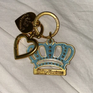 Juicy Couture - nyckelring i babyblå färg - Superfin nyckelring från Juicy Couture med en blå krona och hjärtformade detaljer i guld. Perfekt accessoar för att ge dina nycklar en lyxig touch. Den har en snygg kombination av färger och är både stilren och trendig. Nypris 250 kr, sparsamt använd så i nyskick. 