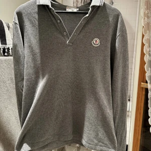 Grå pikétröja från Moncler - Säljer en snygg grå pikétröja från Moncler i mycket bra skick. Tröjan har en klassisk krage med knappar och Monclers logga på bröstet.  Storlek (XL) men väldigt liten i storleken så passar storlek (M).