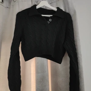 Svart stickad croppad tröja från ONLY - Säljer en snygg svart stickad tröja från ONLY i storlek S. Den är croppad med en cool krage och knappar framtill. Perfekt för höst och vinter, och den har långa ärmar som håller dig varm. Passar både till vardags och festliga tillfällen!