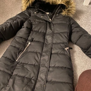 Svart dunjacka från H&M strl 152 - Säljer en svart dunjacka från H&M i storlek M. Jackan har en mysig fuskpäls på huvan och praktiska dragkedjor på fickorna. Perfekt för kalla vinterdagar! 🖤