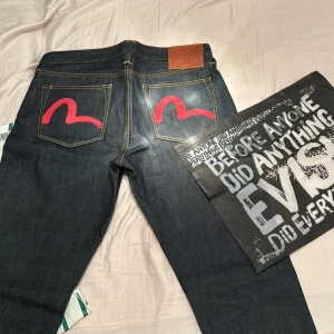 Mörkblå jeans från Evisu - Säljer ett par snygga mörkblå jeans från Evisu med den ikoniska röda måsloggan på bakfickorna. Jeansen har en klassisk design och en läderpatch med Evisu-logga. Perfekta för dig som vill ha en unik stil! 🕶️väldigt eftertraktade, använda max 3 gånger därav helt nytt skick, kvitto finns dessutom från hemsidan som jag köpt jeansen ifrån