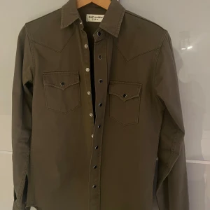 Saint Laurent tröja/overshirt - Saint Laurent overshirt köpt för ca 1 månad sedan i USA från deras affär. Storlek är XS men passar mig och jag är 185 och väger ca 65 kg. Ny pris är ca 10 000 vilket gör detta ett kap! Kvitto och tags finns självklart. Hör av dig ifall frågor finns!