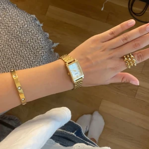Elegant guldfärgad klocka - Säljer en elegant guldfärgad klocka med rektangulär urtavla och länkarmband. Perfekt för både vardag och festliga tillfällen. Klockan har en stilren design som passar till alla outfits. Den är i mycket bra skick och redo att bäras av sin nya ägare.
